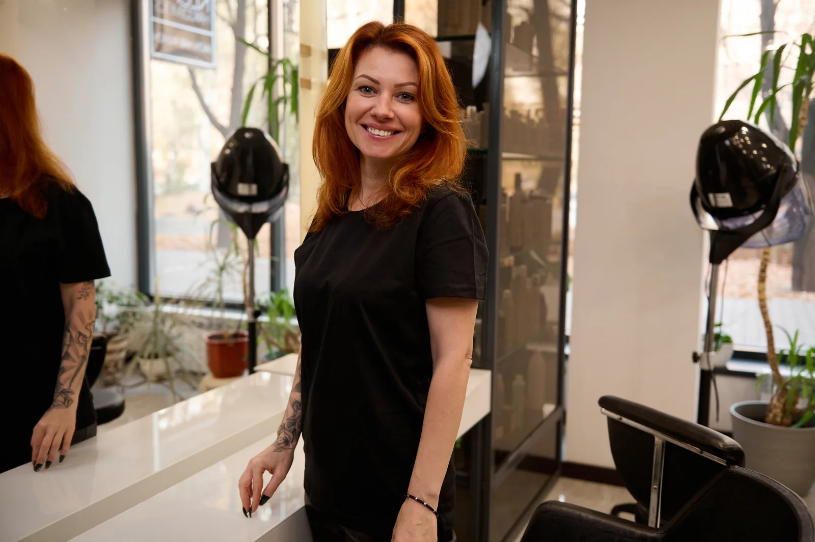 Peluquera con uniforme negro junto al espejo de su salón